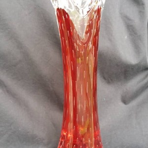 May include: A tall, red glass vase with a textured, bubbled surface. The vase has a unique, open, V-shaped top.
