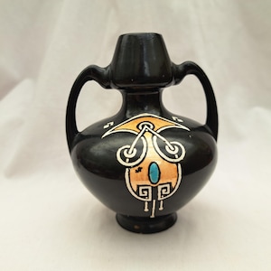 May include: A small black ceramic vase with two handles and a geometric design in gold and blue.