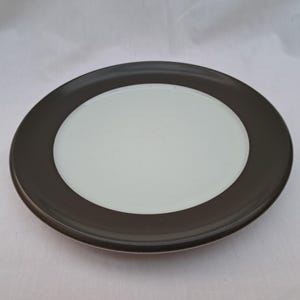 Op de afbeelding: Een wit keramiek bord met een donkerbruine rand. Het bord is rond en heeft een glad oppervlak.