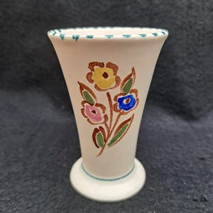 Puede incluir: Un jarrón de cerámica blanco con un diseño floral verde, marrón, amarillo, rosa y azul.