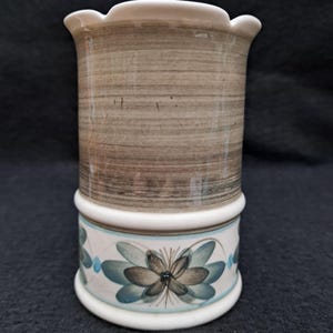 May include: A white ceramic vase with a brown and blue floral design. The vase has a wide mouth and a narrow base.