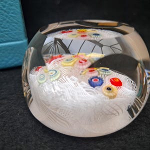 May include: A clear glass paperweight with a white, swirling design and colorful glass flowers inside.