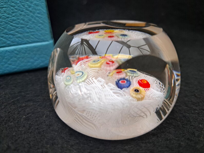 May include: A clear glass paperweight with a white, swirling design and colorful glass flowers inside.