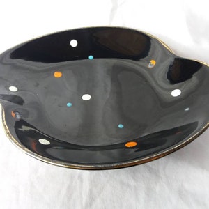 May include: A black ceramic dish with a gold rim and a scattered pattern of white, orange, and blue dots.