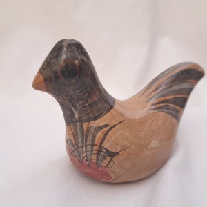 May include: A ceramic bird figurine with a tan body, black head, and orange beak. The bird has black and tan markings on its wings and tail, and red accents on its chest. The figurine is a decorative item.