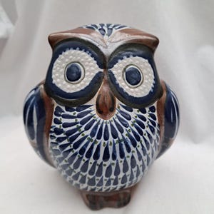 Könnte beinhalten: Keramik-Eulenfigur mit detailliertem Design. Die Eule hat einen braunen Kopf und Akzente, große weiße Augen und einen blau-weiß gemusterten Körper. Die Figur ist ein dekorativer Gegenstand.