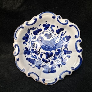 May include: A white ceramic dish with a scalloped edge and a hand-painted blue design. The centre features a bird surrounded by floral motifs, while the rim is decorated with blue scrollwork patterns. The dish has a glossy finish throughout.