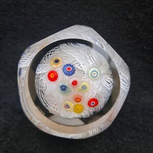 May include: A clear glass paperweight with a white swirl design and colorful flowers inside. The paperweight is shaped like a hexagon.