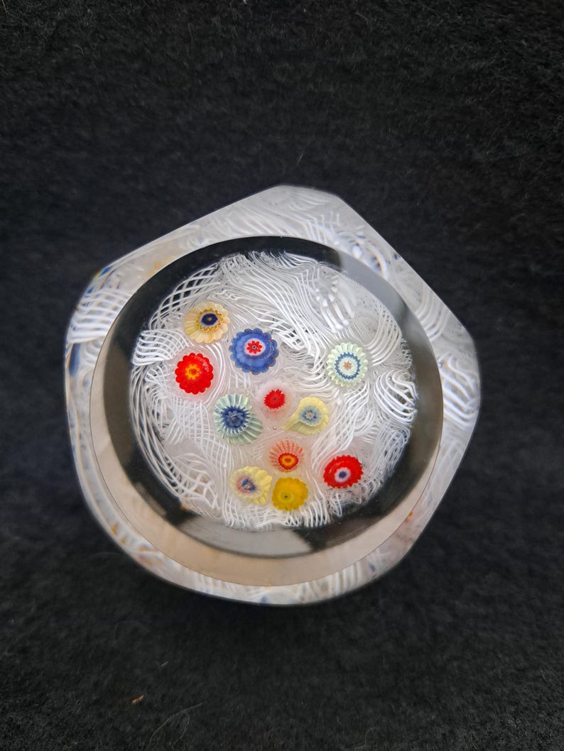 May include: A clear glass paperweight with a white swirl design and colorful flowers inside. The paperweight is shaped like a hexagon.