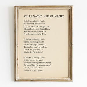 May include: A framed print of the German Christmas carol "Stille Nacht, Heilige Nacht" (Silent Night, Holy Night). The lyrics are printed in black ink on a cream-colored background.
