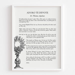 Pode incluir: Uma impressão emoldurada com o texto da oração "Adoro Te Devote" de São Tomás de Aquino. O texto preto está sobre um fundo branco, com uma ilustração detalhada de um ostensório e um desenho de raios de sol. A impressão está em uma moldura branca.