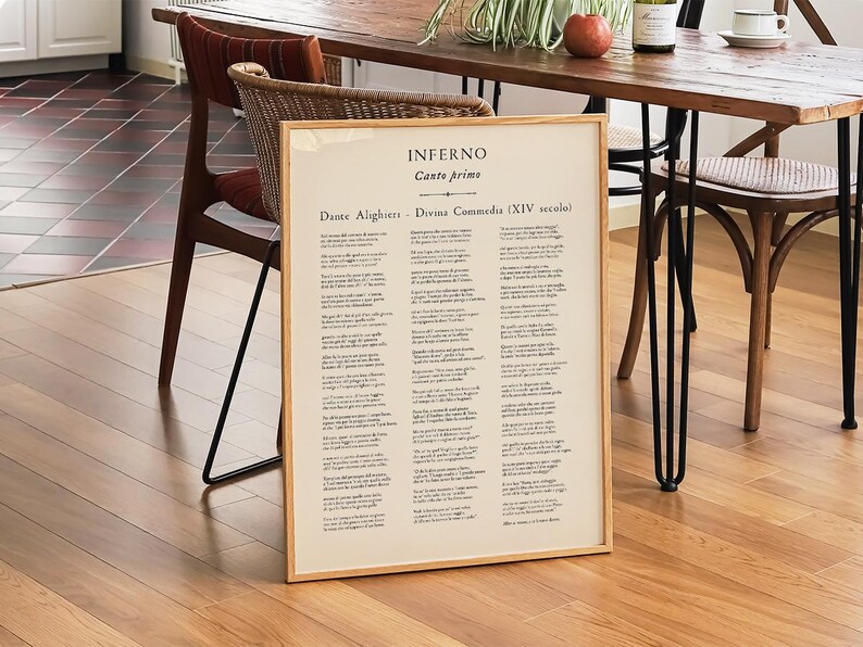 May include: A framed print of Dante Alighieri's Inferno, Canto Primo, in Italian. The text is displayed on a cream-colored background with a light brown wooden frame. The print is leaning against a wooden floor.
