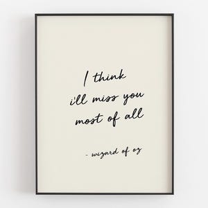 以下が含まれることがあります： 「I think I'll miss you most of all」というオズの魔法使いからの引用句が書かれた額入りのアートプリント。黒の手書き風の文字がクリーム色の背景にあり、黒いフレームに入っています。