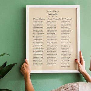 May include: A framed print of Dante Alighieri's Inferno, Canto Primo, from the Divine Comedy. The text is in Italian, set against a cream-colored background, and framed in a white border. The print is held against a green wall.