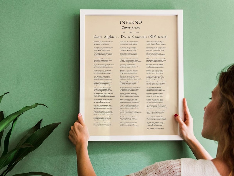 May include: A framed print of Dante Alighieri's Inferno, Canto Primo, from the Divine Comedy. The text is in Italian, set against a cream-colored background, and framed in a white border. The print is held against a green wall.