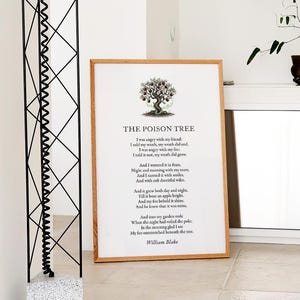 May include: A framed print of William Blake's poem "The Poison Tree" with a tree illustration. The artwork has a light brown wooden frame and is displayed on a light-coloured surface. A decorative plant in a brown pot is visible in the background.