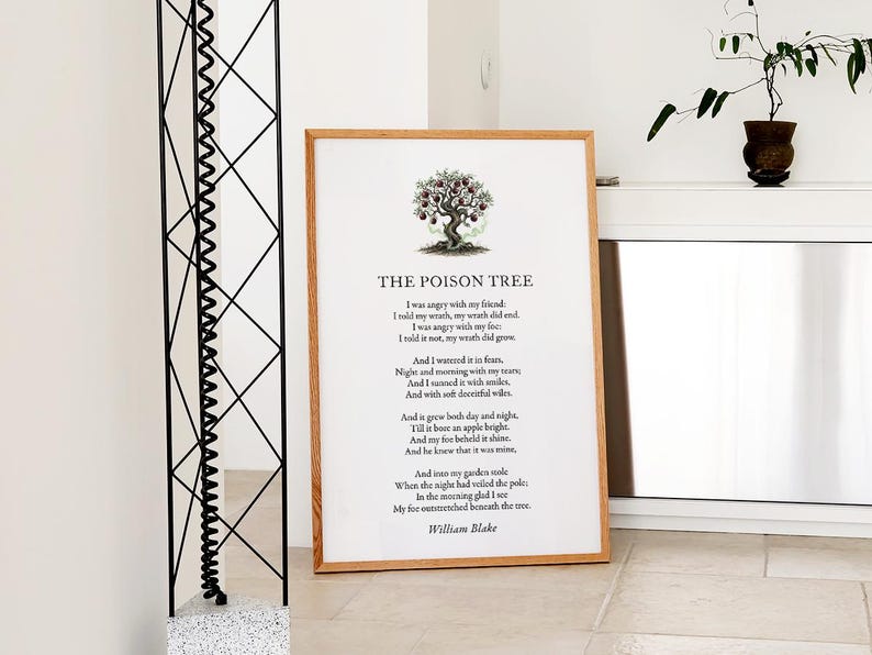 May include: A framed print of William Blake's poem "The Poison Tree" with a tree illustration. The artwork has a light brown wooden frame and is displayed on a light-coloured surface. A decorative plant in a brown pot is visible in the background.