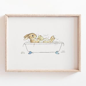 May include: A framed print featuring a watercolor illustration of a brown rabbit relaxing in a vintage bathtub filled with bubbles. The rabbit is holding a yellow sponge. The tub has blue feet.