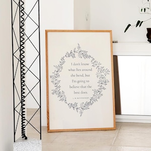 K&ouml;nnte beinhalten: Ein gerahmter Druck mit einem hellen Holzrahmen. Der Druck zeigt einen floralen Kranz, der den Text umgibt: "I don't know what lies around the bend, but I'm going to believe that the best does."