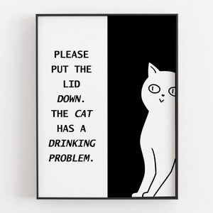 Peut inclure: Une affiche encadrée avec un cadre noir. L'affiche est divisée en deux sections verticales : une section blanche avec le texte "PLEASE PUT THE LID DOWN. THE CAT HAS A DRINKING PROBLEM." et une section noire avec un chat blanc.