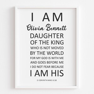 May include: A white framed print with black text that reads "I AM Olivia Bennett DAUGHTER OF THE KING WHO IS NOT MOVED BY THE WORLD FOR MY GOD IS WITH ME AND GOES BEFORE ME I DO NOT FEAR BECAUSE I AM HIS 2 CORINTHIANS 6:18"