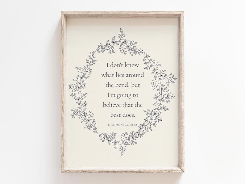 K&ouml;nnte beinhalten: Gerahmter Druck mit hellbeigem Hintergrund und einem Zitat, umgeben von einem floralen Kranz. Das Zitat lautet: &bdquo;Ich wei&szlig; nicht, was um die Ecke liegt, aber ich werde glauben, dass das Beste es tut.&ldquo; Der Autor ist L.M. Montgomery.