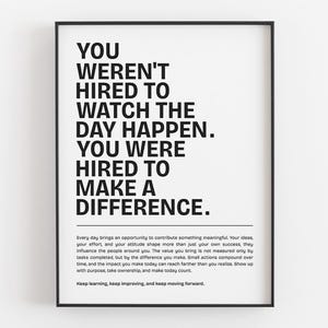 May include: A rectangular wall art print in a black frame featuring bold black text on a white background that reads: YOU WEREN'T HIRED TO WATCH THE DAY HAPPEN. YOU WERE HIRED TO MAKE A DIFFERENCE. Below this, smaller text provides additional motivational advice.