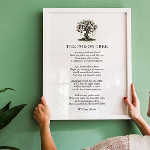 May include: A framed print of William Blake's poem "The Poison Tree" with a tree illustration. The poem is printed in black on a white background. The white frame is held against a green wall.