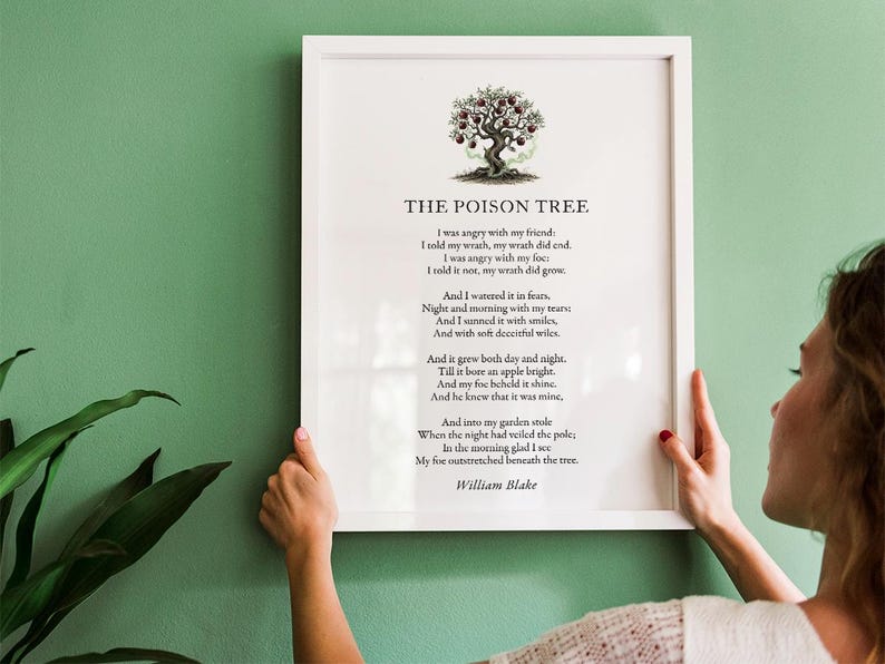 May include: A framed print of William Blake's poem "The Poison Tree" with a tree illustration. The poem is printed in black on a white background. The white frame is held against a green wall.