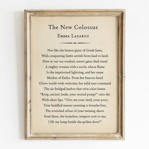 May include: A framed print featuring the poem "The New Colossus" by Emma Lazarus. The text is in a classic serif font on a cream-colored background, framed by a distressed, light-brown wooden frame. The poem is centered and includes the author's name.