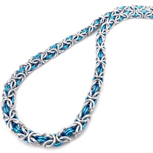 May include: A silver and blue byzantine chain necklace. The necklace is made of interlocking metal rings, with a bright blue center and silver outer rings. The chain is displayed on a white background.