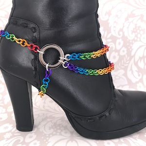 May include: A pair of black leather boots with a rainbow chain ankle bracelet. The bracelet has a silver ring and a star charm.