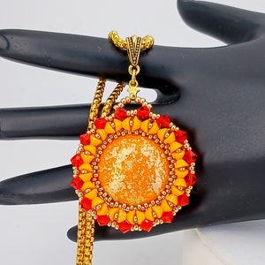 May include: A round pendant necklace featuring a central orange cabochon with gold flecks, surrounded by a circular border of alternating bright yellow and red faceted crystal beads, suspended from a gold-toned chain with a decorative metal bail.