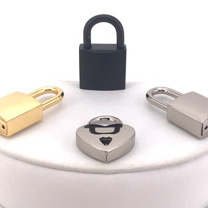 May include: Four small padlocks in different colors and styles. A black padlock, a gold padlock, a silver padlock, and a heart-shaped silver padlock.