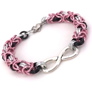 Peut inclure: Bracelet fait à la main avec un motif de cotte de mailles, composé de maillons roses, argentés et noirs. Il comprend un symbole infini argenté et une fermeture à fermoir. Ce bijou est adapté au quotidien.