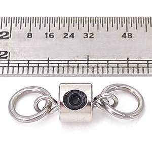 May include: A silver swivel snap with a black center piece. The snap is about 1 inch long and is shown next to a ruler.