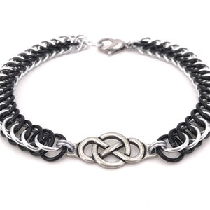 Puede incluir: Un brazalete de cadena negro y plateado con un dije de nudo celta plateado.