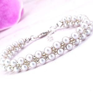 May include: A delicate silver bracelet with a double row of white pearls and silver beads. The bracelet has a silver clasp.