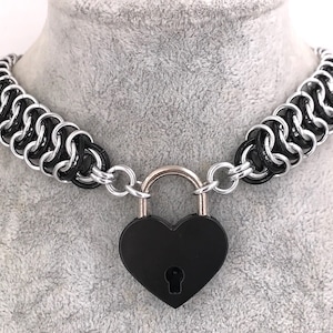 Peut inclure: Un collier ras de cou en maille noire et argent avec un cadenas en forme de cœur noir.