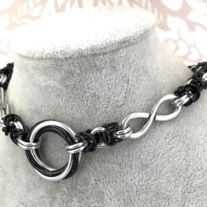 May include: A black and silver metal choker necklace with an infinity symbol and a large ring in the center.