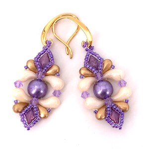May include: A pair of dangle earrings with a gold hook and a purple, white, and gold beaded design.
