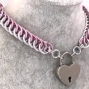 Peut inclure: Un collier ras de cou en maille de chaîne argentée et rose avec un cadenas en forme de cœur argenté.