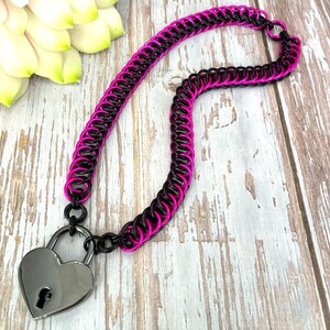 Peut inclure: Un collier en cotte de mailles noir et rose avec un fermoir cadenas en forme de cœur. Le collier est composé d'anneaux métalliques imbriqués, avec des anneaux noirs et roses alternés. Le cadenas en forme de cœur est de couleur argent.