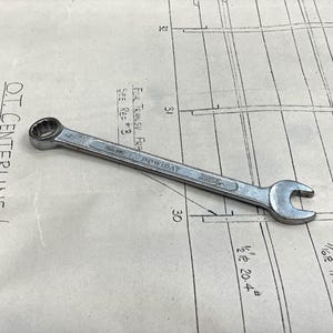 May include: A silver wrench with a black handle. The wrench is lying on a piece of paper with a grid pattern and text that reads "O.T. CENTERLINE LONGITUDIN FRAMES 22-41 - LOOKING", "FOR TRANSV FRA SEE REF 3", "7/16R 17.85", "1/2R 20.4", "32", "31", and "30".