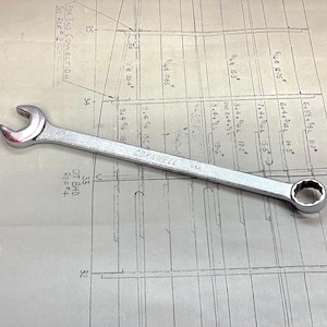 May include: A silver wrench with a 1/2 inch drive and a 13/16 inch opening. The wrench is made by the company "Cornwell" and is lying on a blueprint.