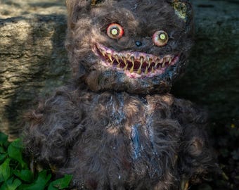 Könnte beinhalten: Ein unheimlicher, brauner Teddybär mit einem bedrohlichen Grinsen und scharfen Zähnen. Der Bär hat rote Augen und Krallen, was ihm ein erschreckendes Aussehen verleiht. Das Fell ist verfilzt und verfärbt, was die beunruhigende Ästhetik verstärkt.