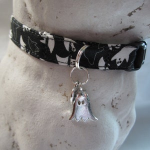 Puede incluir: Collar de perro con estampado de fantasmas en blanco y negro con un dije de fantasma plateado.