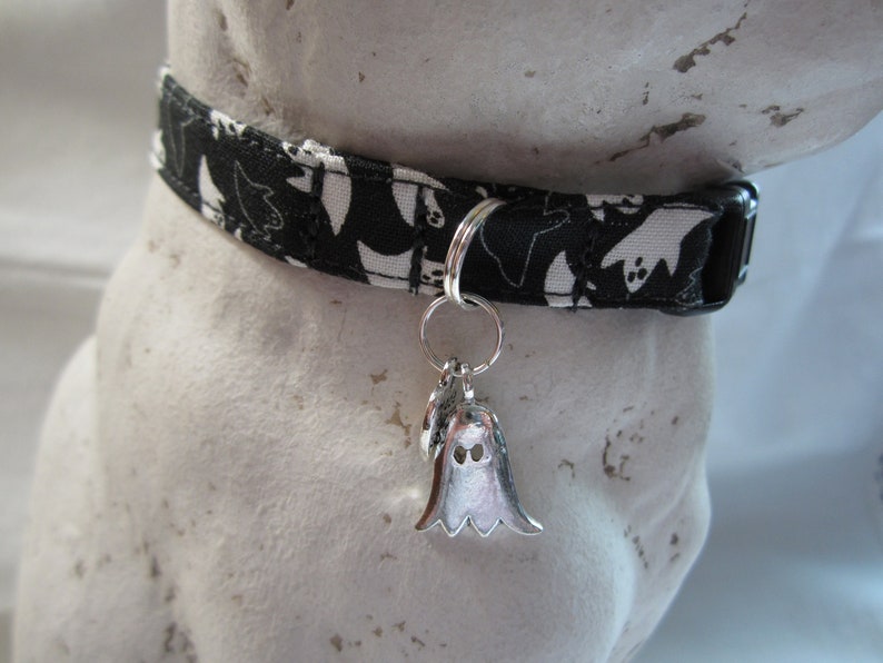 Puede incluir: Collar de perro con estampado de fantasmas en blanco y negro con un dije de fantasma plateado.