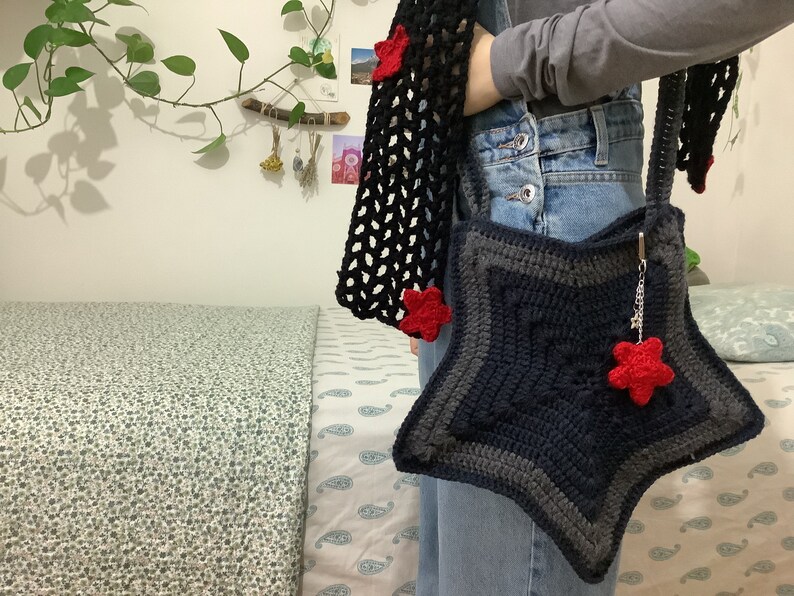 May include: A blue and gray crocheted star-shaped bag with a red star charm. The bag is worn over the shoulder and has a black crocheted strap.