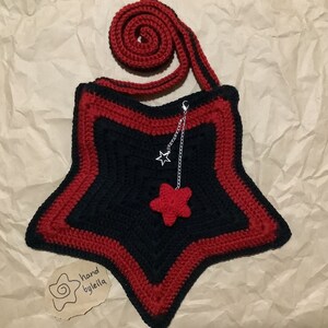 May include: A black and red crocheted star-shaped bag with a red star charm and a silver chain. The bag has a red crocheted strap. The tag says "hand by leila".